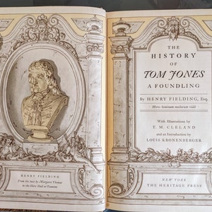 May include: A vintage book cover with an ornate design featuring a bust of Henry Fielding, the author of "The History of Tom Jones, a Foundling". The cover is in shades of brown and yellow.