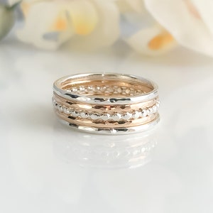 May include: A set of five stacking rings in silver and rose gold. The rings are textured and have a beaded design.