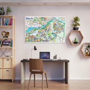 May include: A colorful map of Anaheim Hills, California, with a light blue river running through it. The map is framed and hanging on a white wall above a desk with a laptop, a chair, and a lamp.