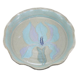 May include: A ceramic pie dish featuring a light blue and purple flower design. The dish has a wavy edge and a light grey background.