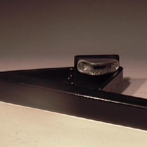 May include: A black metal bracket with a silver metal latch. The bracket is designed to be mounted to a wall or other surface.