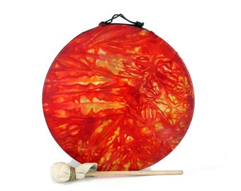 Puede incluir: Un tambor de mano rojo y amarillo con un mazo de madera. El tambor tiene un patrón de teñido anudado.