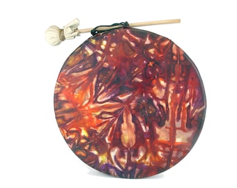 Puede incluir: Un tambor redondo pintado a mano con un diseño abstracto colorido en tonos de rojo, naranja, morado y amarillo. El tambor está hecho de cuero y tiene un palo de madera para tocar.