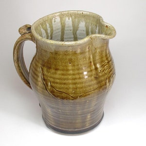 May include: A brown ceramic pitcher with a wide mouth and a handle. The pitcher has a light brown glaze with a white drip pattern.