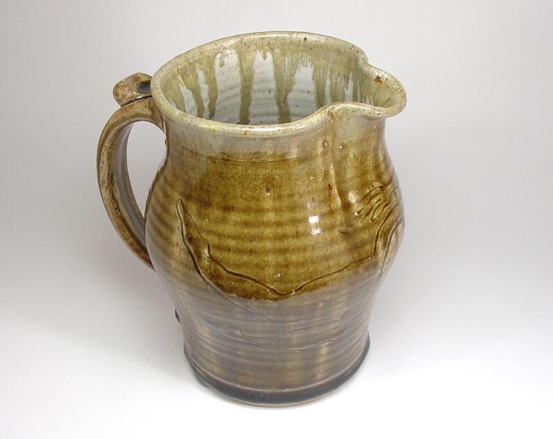 May include: A brown ceramic pitcher with a wide mouth and a handle. The pitcher has a light brown glaze with a white drip pattern.