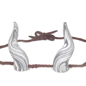 Peut inclure: Une paire de cornes en spirale blanches et grises avec un bandeau en cordon marron. Les cornes sont faites d'un matériau lisse et texturé.