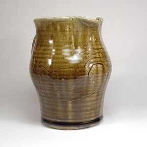 May include: A brown ceramic pitcher with a white glaze design. The pitcher has a wide base and a narrow neck.