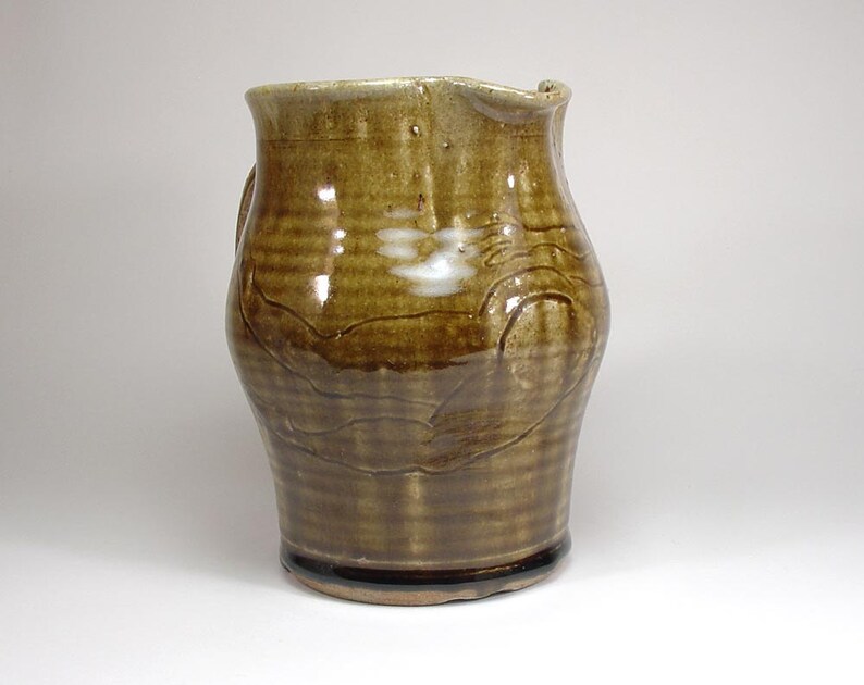 May include: A brown ceramic pitcher with a white glaze design. The pitcher has a wide base and a narrow neck.