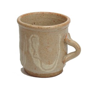 May include: A beige ceramic mug with a white glaze and a unique, wavy design. The mug has a rounded handle.