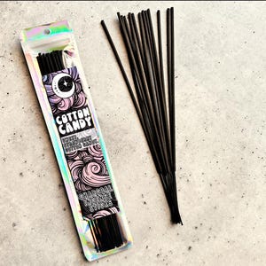 May include: A package of charcoal incense sticks with a cotton candy scent. The package is iridescent and features the words "Cotton Candy" and "Sweet Strawberry Cotton Candy." Several loose incense sticks are next to the package.