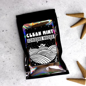 May include: A black pouch with a holographic iridescent finish containing brown incense cones. The pouch has a white label with the text "Clean Mint Incense Cones" and a black and white illustration of a boat on waves.