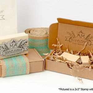 May include: A wooden stamp with the text "MA ЗАМ АЙНА THARACTE" in a decorative banner with leaves. The stamp is in a brown box with a burlap and turquoise lace ribbon. The box is next to a larger brown box with a similar design and the text "AM ANNA MARIE PHOTOGRAPHY".