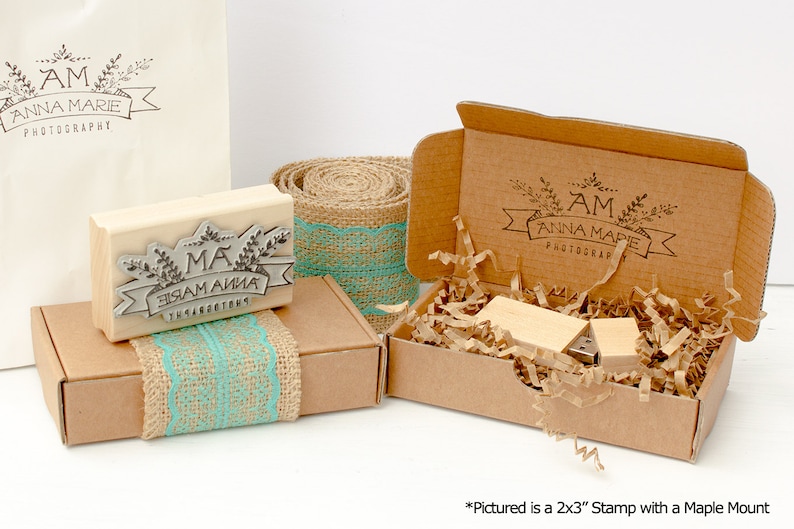 May include: A wooden stamp with the text "MA ЗАМ АЙНА THARACTE" in a decorative banner with leaves. The stamp is in a brown box with a burlap and turquoise lace ribbon. The box is next to a larger brown box with a similar design and the text "AM ANNA MARIE PHOTOGRAPHY".