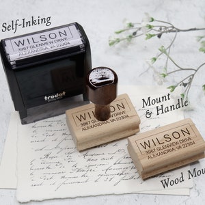 May include: Three wooden self-inking stamps with the text "WILSON 3967 GLENVIEW DRIVE ALEXANDRIA, VA 22304" on each. The stamps are shown on a white surface with a piece of paper with handwritten text underneath. The top stamp is a black self-inking stamp with a trodat logo. The middle stamp is a wooden stamp with a brown handle. The bottom stamp is a wooden stamp with no handle. The text "Self-Inking", "Mount & Handle", and "Wood Mount" are written above each stamp.