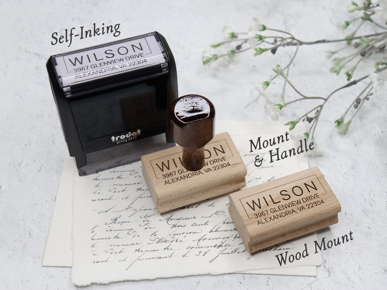 May include: Three wooden self-inking stamps with the text "WILSON 3967 GLENVIEW DRIVE ALEXANDRIA, VA 22304" on each. The stamps are shown on a white surface with a piece of paper with handwritten text underneath. The top stamp is a black self-inking stamp with a trodat logo. The middle stamp is a wooden stamp with a brown handle. The bottom stamp is a wooden stamp with no handle. The text "Self-Inking", "Mount & Handle", and "Wood Mount" are written above each stamp.