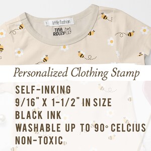 May include: A beige t-shirt with a bee and daisy pattern. The shirt has a label that says "little fashion" and "TINA RIDLEY". The text below the shirt reads "Personalized Clothing Stamp", "SELF-INKING", "9/16" X 1-1/2" IN SIZE", "BLACK INK", "WASHABLE UP TO 90&deg; CELCIUS", and "NON-TOXIC".