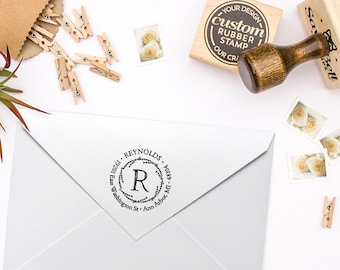 Puede incluir: Un sello de goma redondo, en blanco y negro, con el texto "10261 REYNOLDS" y "R" en un diseño de corona. El sello está en un sobre blanco.