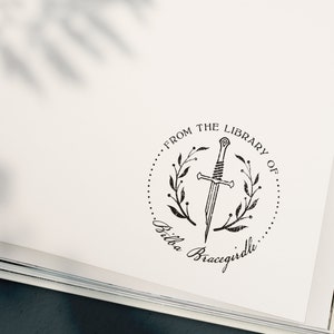 May include: A black and white illustration of a sword in a wreath with the text "From the Library of... Bella Bracigirdle"