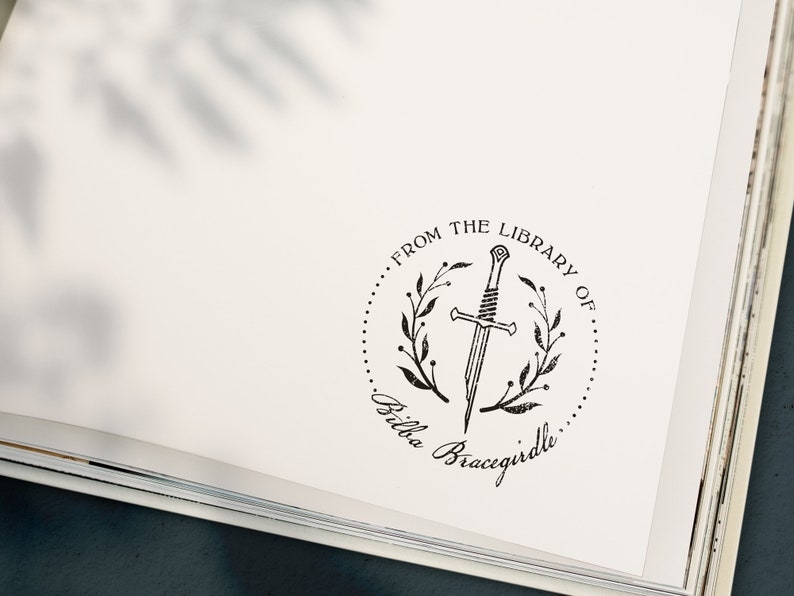 May include: A black and white illustration of a sword in a wreath with the text "From the Library of... Bella Bracigirdle"