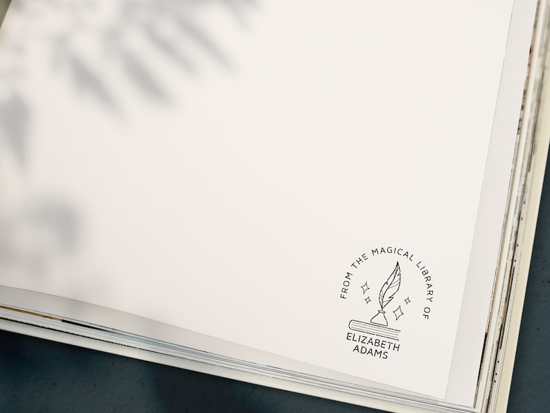 May include: A white book with a black and white stamp that reads "From the Magical Library of Elizabeth Adams". The stamp features a quill pen and a book with stars.
