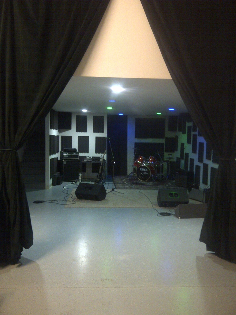 May include: A black drum set with a white drum head and a black microphone stand in a room with black soundproof panels on the walls.