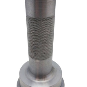 Pu&ograve; includere: Un utensile in metallo color argento con un manico cilindrico e una base circolare piatta. Il manico presenta un motivo strutturato, a tratteggio incrociato, per una presa migliore. L'utensile sembra essere un articolo specializzato, forse per scopi industriali o artigianali.