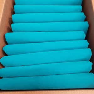 May include: A cardboard box filled with a stack of teal blue fabric squares.