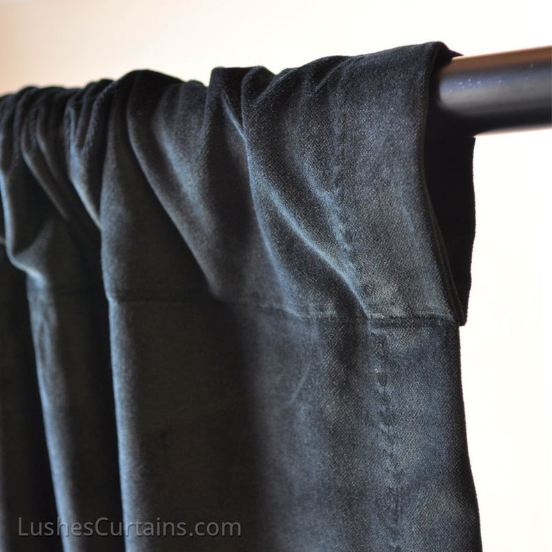 May include: Close-up of a black velvet curtain hanging from a black curtain rod. The curtain is gathered at the top and has a smooth, luxurious texture.