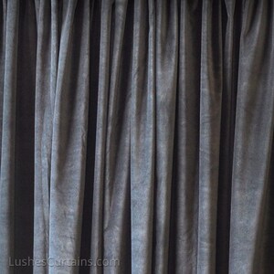 May include: A close-up of a dark gray velvet curtain with pleats. The fabric has a soft, textured appearance.