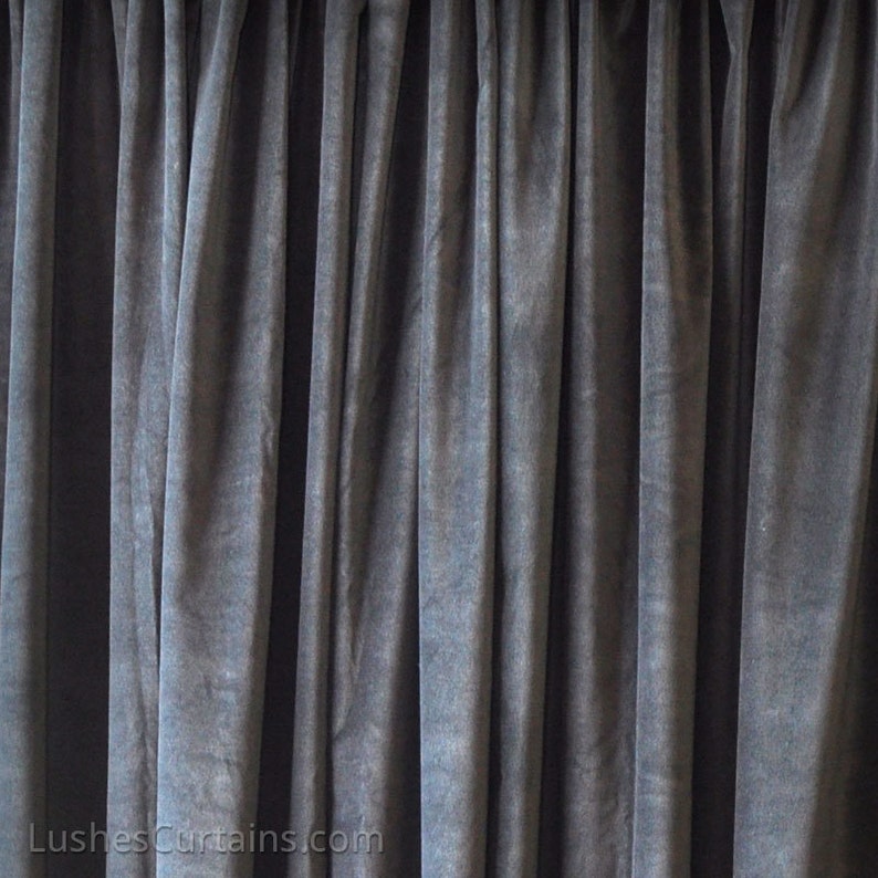 May include: A close-up of a dark gray velvet curtain with pleats. The fabric has a soft, textured appearance.