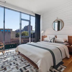 May include: A white bed with a gray blanket and white pillows in a modern bedroom with a wooden headboard, a round mirror, and a wood floor.