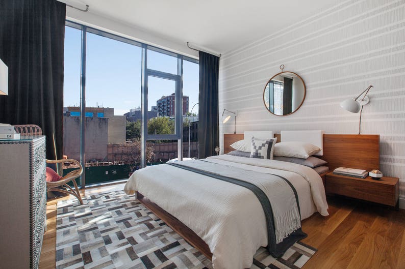 May include: A white bed with a gray blanket and white pillows in a modern bedroom with a wooden headboard, a round mirror, and a wood floor.