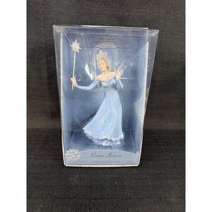 May include: A Hallmark Keepsake Ornament featuring a Queen Aurora figurine in a clear plastic display box. The figurine wears a light blue gown with lavender trim and holds a white star-topped wand. The box text reads Queen Aurora.