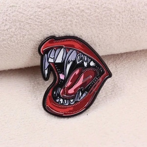 May include: A red and black enamel pin with a detailed illustration of a large, open mouth with sharp teeth and a red tongue.