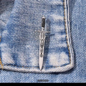 May include: A silver-colored dagger pendant with a black handle and intricate design on the blade. The pendant is set against a blue denim background. The text "Color: Polychrome" is visible.