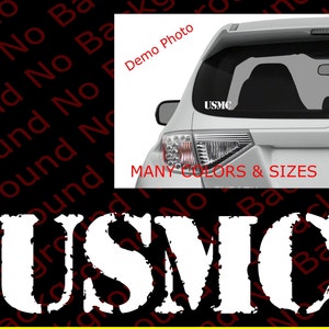 May include: White vinyl decal with a distressed font that reads "USMC". The decal is shown on the back window of a silver car. The text "MANY COLORS & SIZES" is also visible in the image.