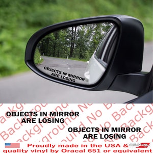 May include: A white car side view mirror with a black sticker that reads "OBJECTS IN MIRROR ARE LOSING".
