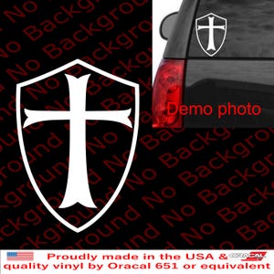 May include: White vinyl decal featuring a shield with a cross design. The decal is shown on a car window, with a "Demo photo" label. The text "Proudly made in the USA" is also visible.