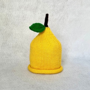May include: A yellow knitted hat shaped like a lemon with a green leaf on top.