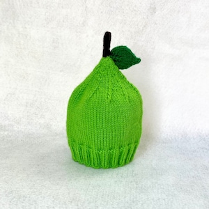 May include: A green knitted hat shaped like a pear with a brown stem and a green leaf on top.