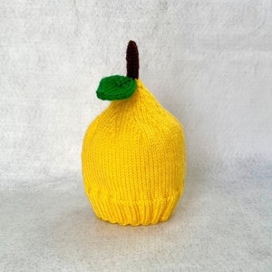 May include: A yellow knitted lemon hat with a green leaf and brown stem.