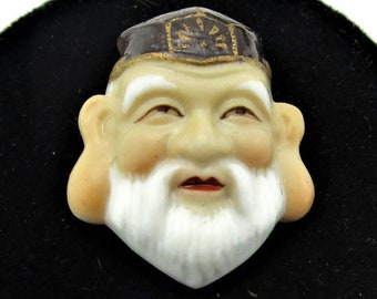 May include: A porcelain figurine of a man with a white beard and a black hat. The figurine has a detailed face with a smiling expression. The figurine is on a black velvet background.