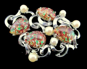 May include: A silver brooch with a swirling design featuring red, green, and gold speckled glass stones and faux pearls.