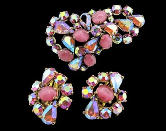 May include: A set of pink and iridescent rhinestone earrings and a brooch. The earrings and brooch are made of gold-toned metal and feature a cluster of pink and iridescent rhinestones.