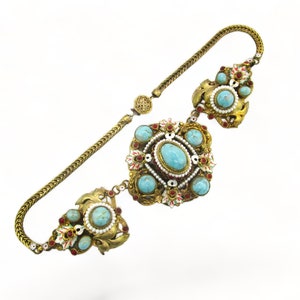 Peut inclure: Un collier en or avec une cha&icirc;ne et trois pendentifs orn&eacute;s. Chaque pendentif pr&eacute;sente une pierre turquoise entour&eacute;e de pierres plus petites et d'accents rouges et blancs.