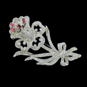 May include: A silver-toned brooch in the shape of a flower with red rhinestone accents.