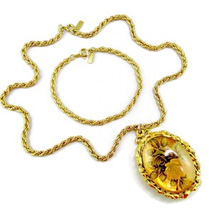 Könnte beinhalten: Eine goldene Kettenkette mit einem passenden Armband. Die Kette hat einen Anhänger mit einem großen ovalen Kamee mit einem floralen Design.