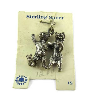 May include: A silver charm depicting two bear figures. The charm is attached to a vintage paper tag with the text "Sterling Silver". The bears have textured fur and are in a playful pose.