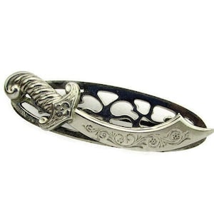 May include: Silver-toned brooch featuring a detailed, ornate, stylized dagger design with floral accents.
