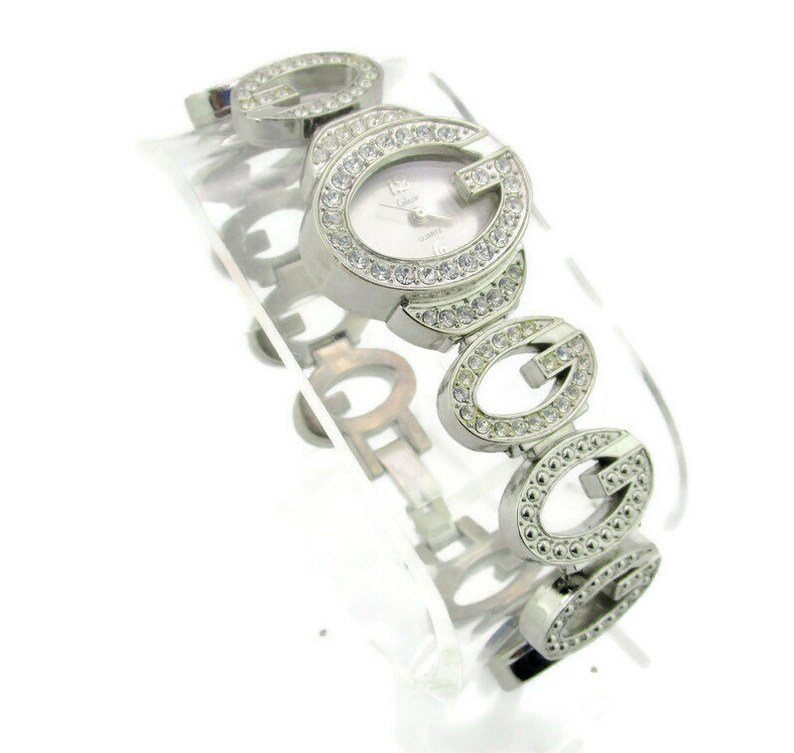 May include: Silver wristwatch with a white face and a band made of interlocking 'G's encrusted with rhinestones.